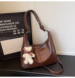 Close-up of dark brown leather hobo bag featuring knotted strap and cute bear charm