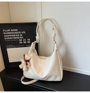 Close-up of cream leather tote bag with knotted shoulder strap and plush bear charm
