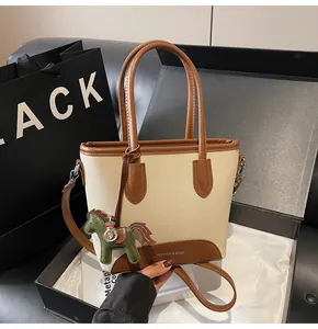 Detalle de bolso cubo de lona con adornos de cuero marrón y colgante de caballo en caja