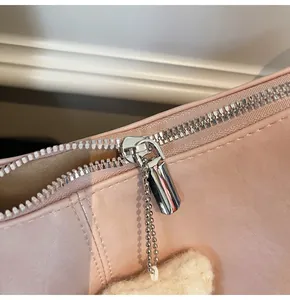 Close-up of pink leather tote bag featuring a silver zipper and plush white pendant