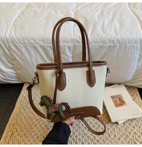 Detalle del bolso de lona con ribete de cuero marrón y colgante de caballo en esterilla