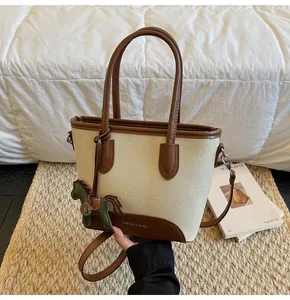 Detalle de bolso tipo cubo de lona crema con ribete de cuero marrón y colgante de caballo