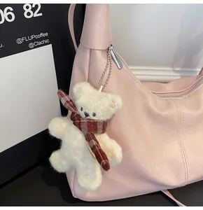 Close-up of a plush cream bear charm with plaid scarf on a soft pink leather shoulder bag