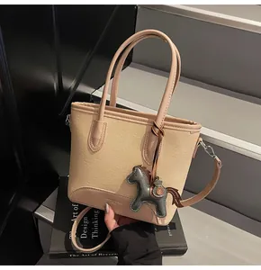 Detalle de bolso tipo cubo de lona con ribete de cuero y colgante de caballo