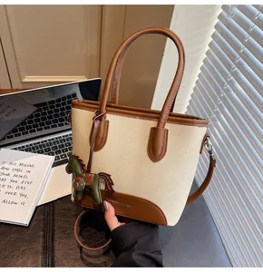Detalle del bolso tote de lona beige con ribete de cuero marrón y colgante de caballo