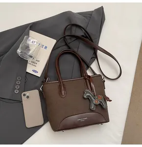 Detalle de bolso tipo cubo de lona marrón oscuro con asas de cuero y colgante de caballo