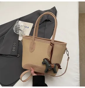 Detalle de bolso tipo cubo en lona caqui y cuero rosa con colgante de caballo y asa