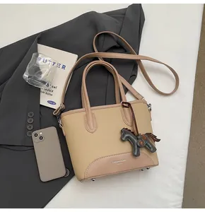 Detalle del bolso tipo cubo de lona beige con ribete de cuero rosa y colgante de caballo
