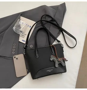 Detalle de bolso cubo negro con pies metálicos, correa delgada y colgante decorativo