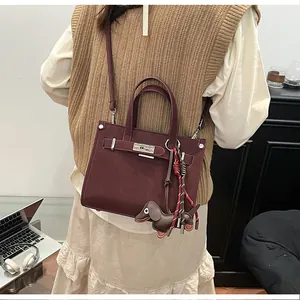 Detail view of burgundy crossbody bag with silver clasp and dachshund charm on model