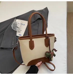 Detalle del bolso de lona beige con ribete de cuero marrón y colgante de caballo