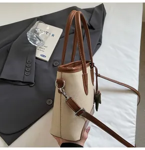 Vista lateral del bolso de lona beige con ribetes de cuero marrón y herrajes plateados