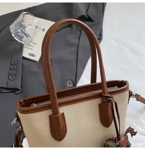 Detalle de cerca de un bolso tipo cubo de lona con ribete de cuero marrón y adorno
