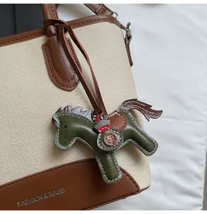 Detalle de colgante de caballo de cuero verde oscuro en un bolso cubo de lona beige y cuero