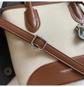 Detalle de lona beige y cuero marrón con hebilla de metal cuadrada plateada del bolso