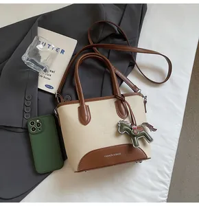 Detalle de bolso cubo de lona con adornos de cuero y colgante de caballo en chaqueta