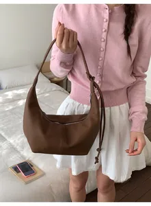 Brown grainy leather crescent bag shown in a cozy bedroom scene with a female model