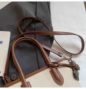 Primer plano de la textura de lona beige y el detalle de la correa de cuero en el bolso