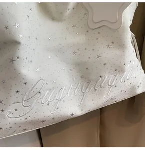Gros plan d'un sac cabas en toile blanche avec broderies d'étoiles argentées et texte