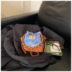 Détail d'un mini sac seau en denim avec chaîne dorée sur fond de blazer noir classique