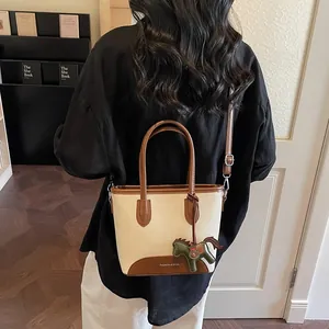 Bolso saco minimalista de lona con ribete de cuero y colgante de caballo en una modelo