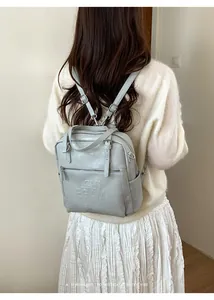 Detail eines hellblauen Kunstleder-Rucksacks mit Silber-Zippern und Logo-Prägung