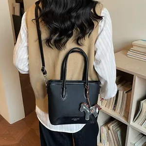 Bolso cubo minimalista de cuero negro con colgante de caballo, mostrado al hombro en interior