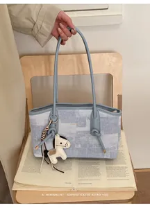 Détail du sac cabas en denim bleu clair avec breloque cheval blanc sur siège en bois