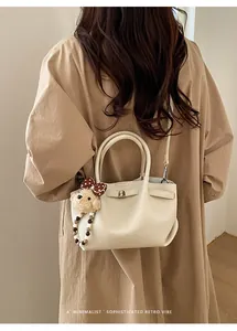 Detail of beige litchi grain bucket bag with cute plush bear pendant and gold lettering
