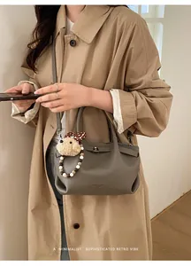 Close-up of grey litchi grain bucket bag with a plush dog charm and detachable strap