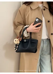 Detail of black textured leather bucket bag with metal lock and cute bear charm pendant
