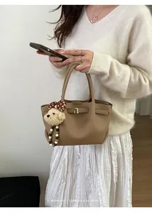 Detail of khaki leather bucket bag with metal clasp and cute plush bear charm