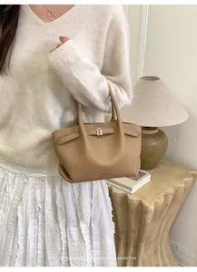 Minimalist khaki leather bucket bag with silver metal buckle held by model in home setting