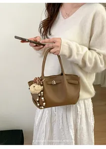 Close-up of brown textured leather bucket bag with cute bear charm and golden hardware