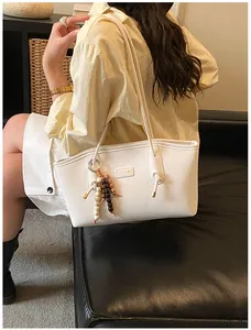 Detailed view of cream tote bag with unique wood bead pendant and metal logo on a sofa