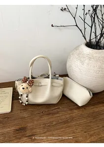 Detail view of beige pebbled leather bucket bag with teddy bear charm on wooden table