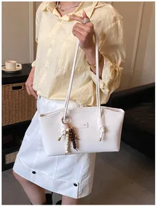 Close-up of white leather tote bag with decorative bead tassel and metal logo detail