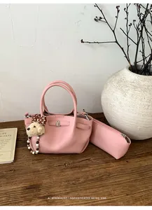 Pink lychee grain bucket bag with matching pouch and plush dog charm on a wooden table