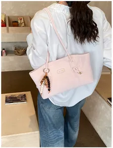 Detail of light pink tote bag with gold metal logo and decorative beaded pendant