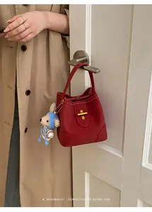 Detail view of red lychee grain bucket bag with gold lock and cute bear charm on door handle