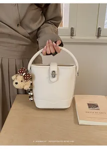 Detail of white lychee leather bucket bag with silver lock and teddy bear charm