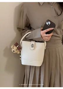 Detail of cream bucket bag with lychee texture, metal twist lock and bear charm