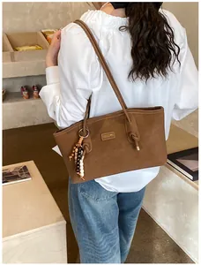 Close-up of brown tote bag with gold logo plaque and beaded tassel charm detail