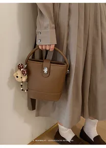 Brown leather bucket bag detail with plush bear charm and metallic silver twist lock