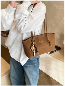 Close-up of brown suede tote bag with wooden bead charm and branded logo detail