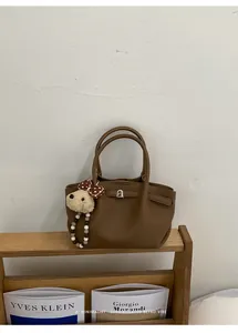 Detail view of brown leather bucket bag with silver metal buckle and cute plush dog charm