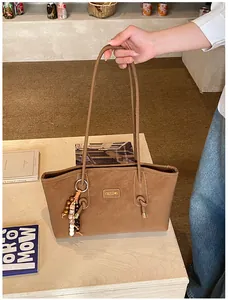 Detail of caramel tote bag with metallic logo plate, beaded tassel, and suede texture