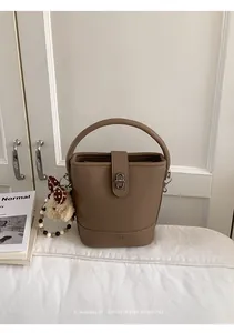 Detail of khaki bucket bag with lychee texture, metal twist lock and plush bear charm