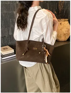 Detail of a brown suede tote bag with slim shoulder straps and vintage beaded pendant