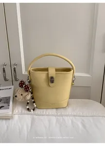 Detail of yellow leather bucket bag with silver twist lock and cute plush bear charm